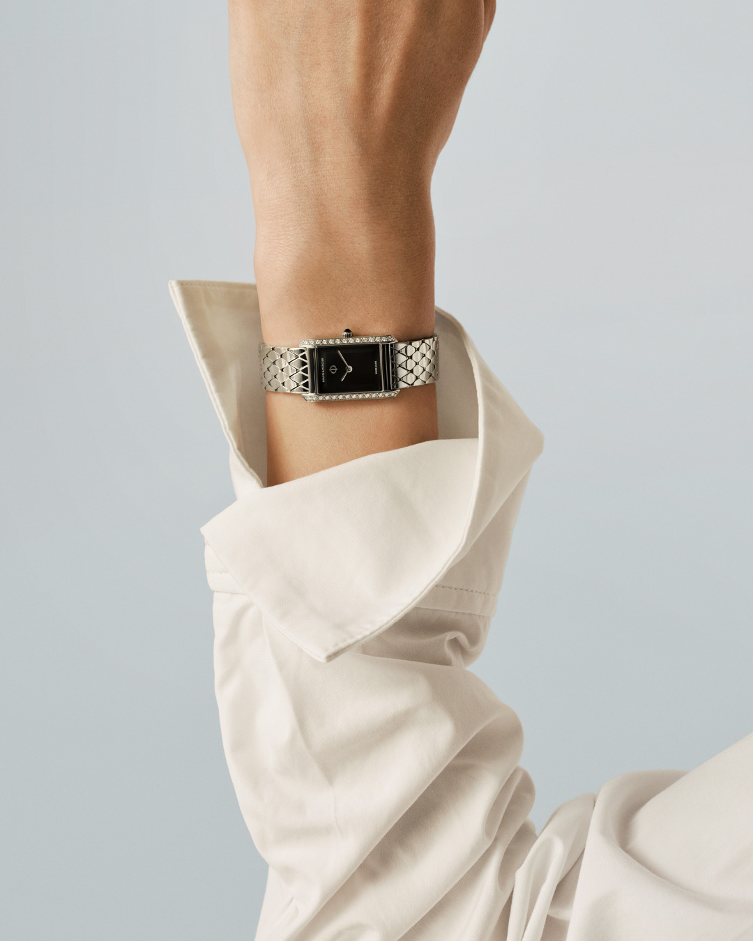 A woman’s wrist emerges from a loose white shirt sleeve. She wears a diamond-set Hampton XS with a black dial. The steel bracelet catches the light against pale skin.